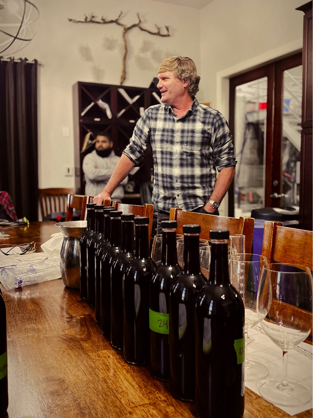 Man standing and smiling behind a table lined with wine bottles during a tasting session