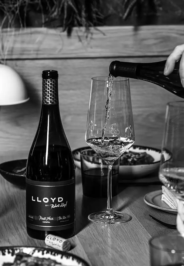 Person pouring Robert Lloyd wines at a dinner table.
