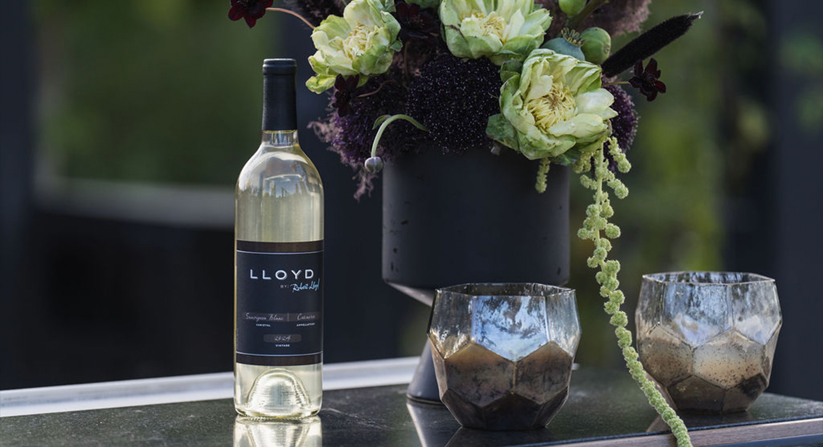 A bottle of Lloyd by Robert Lloyd Sauvignon Blanc sits atop a table with a bouquet of flowers.