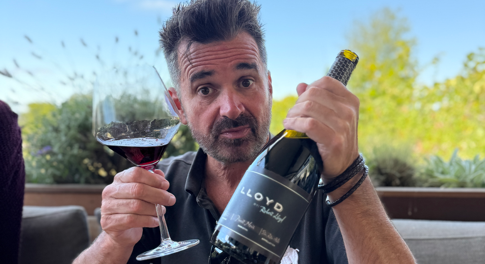 Photo of writer and podcaster Dan Dunn holding a bottle of Lloyd by Robert Lloyd Pinot Noir and a glass of wine.