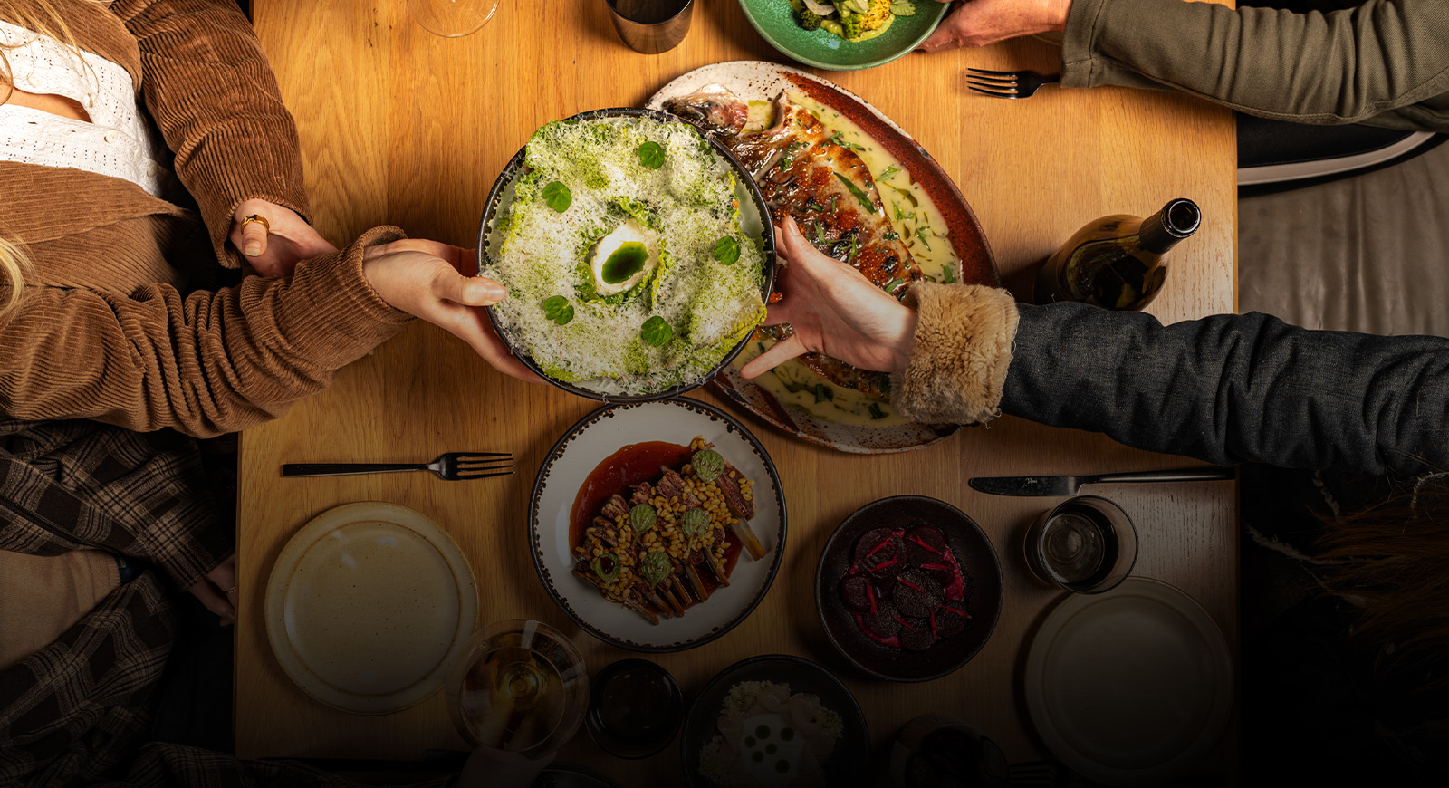 A warm, communal dinner scene with friends sharing seasonal dishes and glasses of wine around a wooden table.