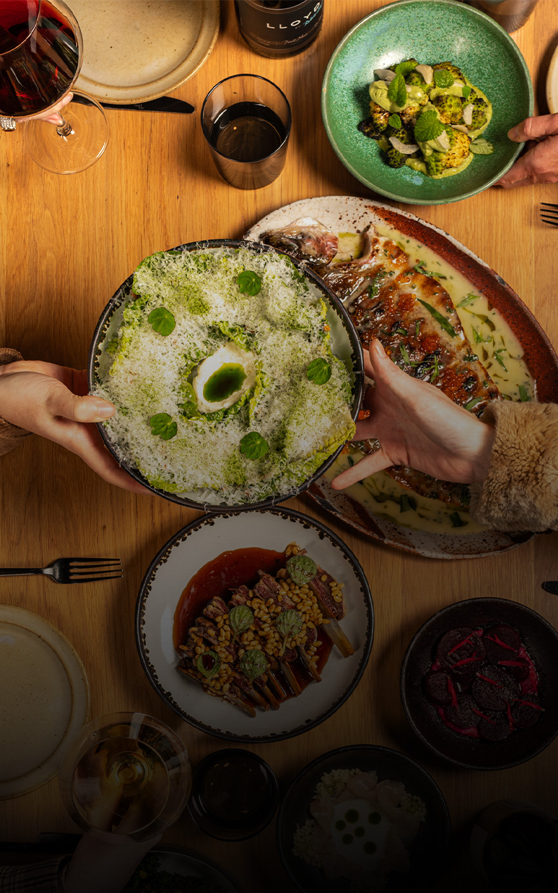 A warm, communal dinner scene with friends sharing seasonal dishes and glasses of wine around a wooden table.