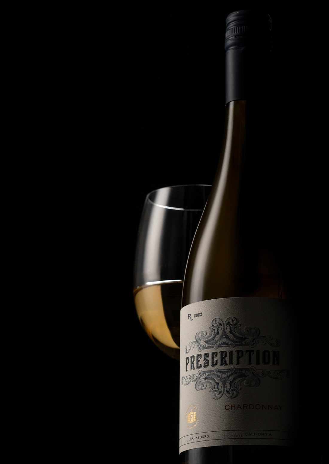 A dimly lit bottle of Prescription Chardonnay with a glass of wine beside it.