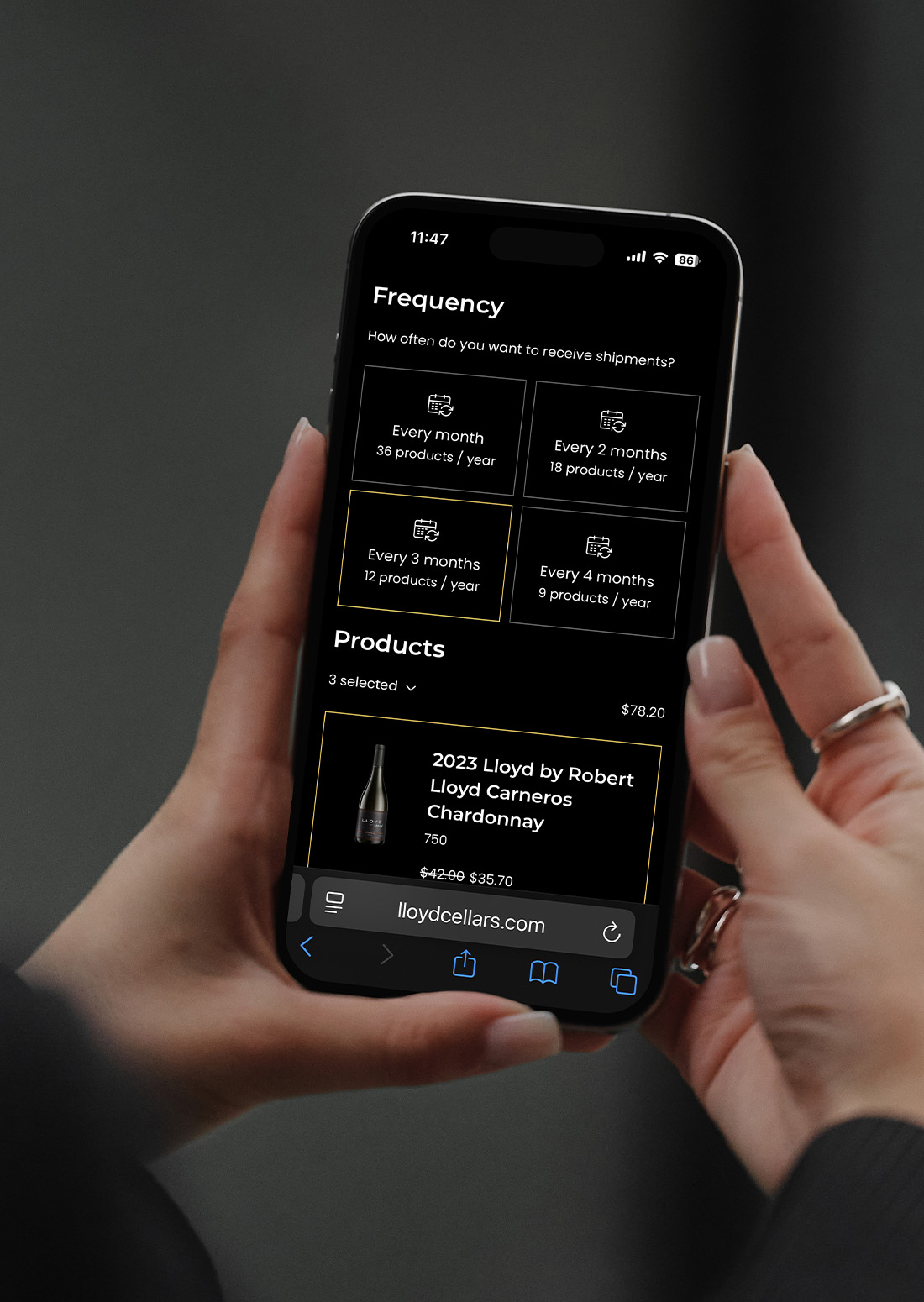 Hand holding a smartphone with the Lloyd Cellars wine subscription interface open, showing customizable delivery frequency and wine selections.