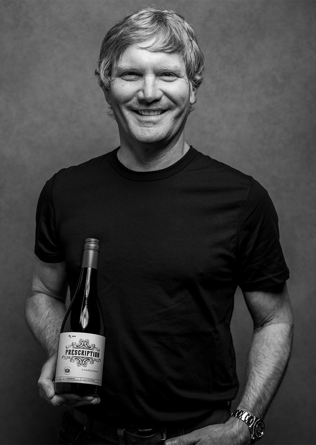 Winemaker Rob Lloyd holding a bottle of Prescription Chardonnay, photographed in black and white.