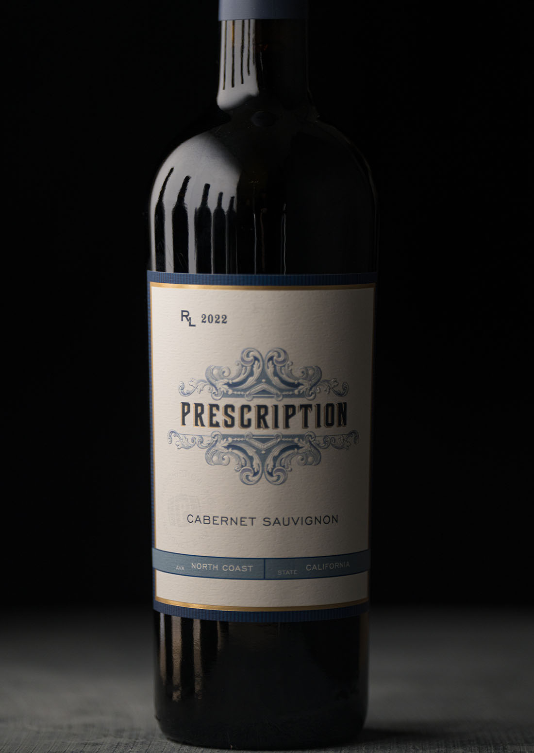 A bottle of Prescription Vineyards 2022 North Coast Cabernet Sauvignon, label featuring ornate blue filigree detailing, shot against a dark background.
